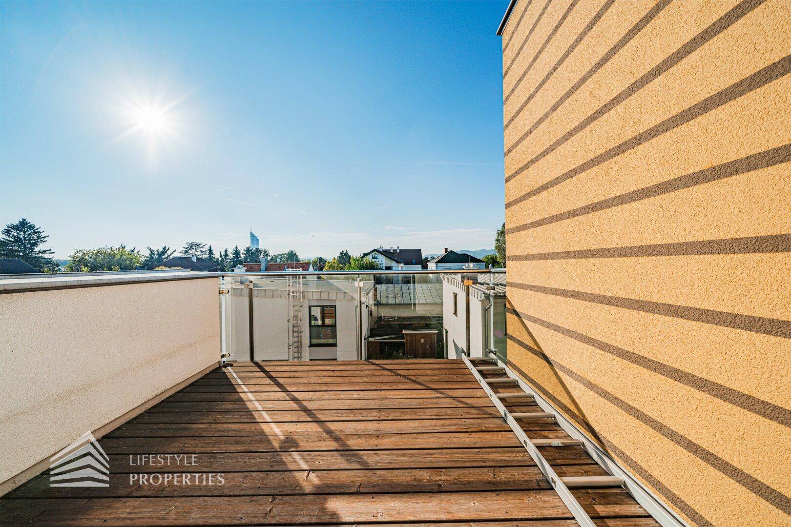 Sonnige Dachterrasse mit Holzboden und moderner Glasbrüstung, bietet einen weiten Ausblick.