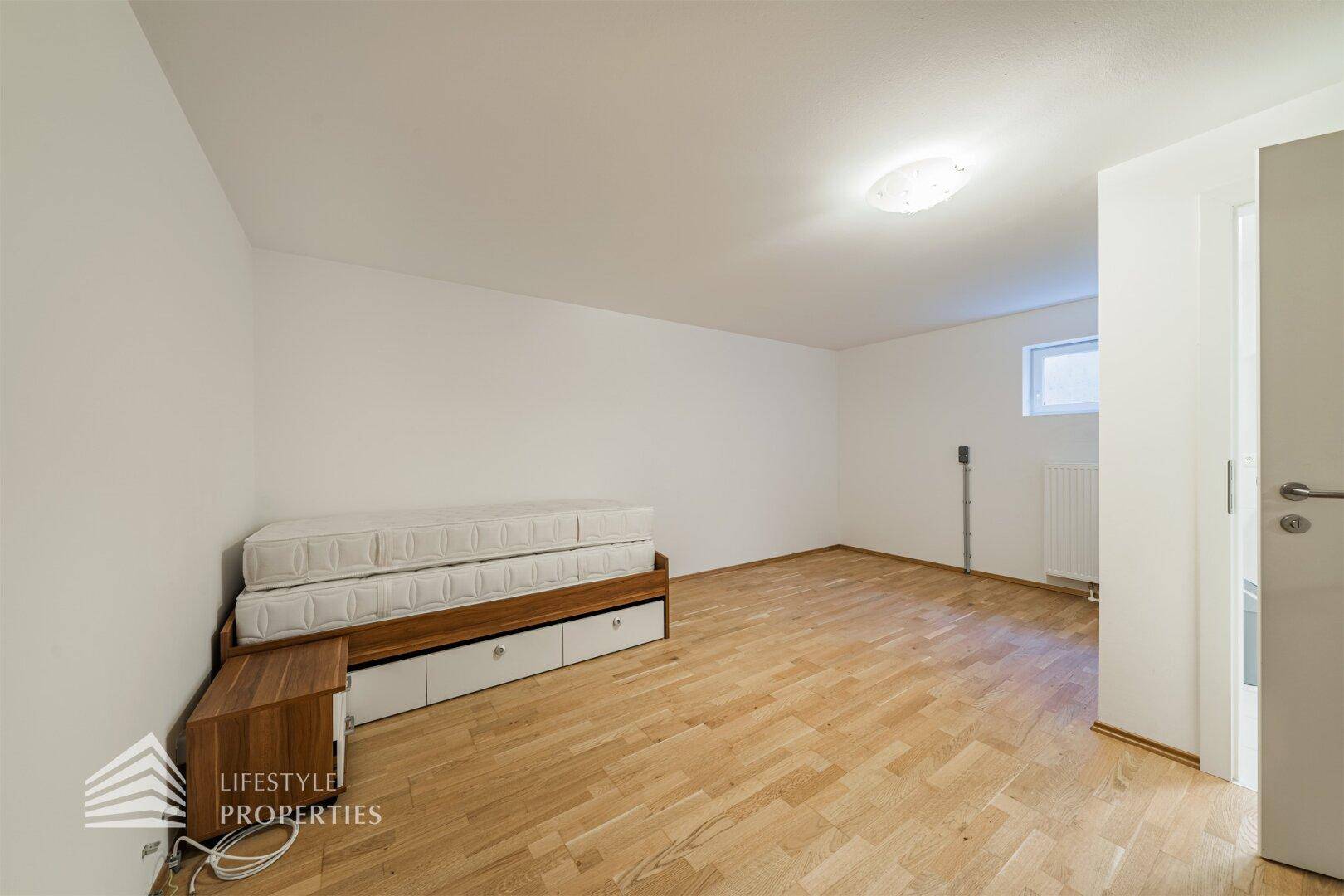 Helles Zimmer im Untergeschoss mit Holzfußboden und einem Bettgestell mit Matratzen.