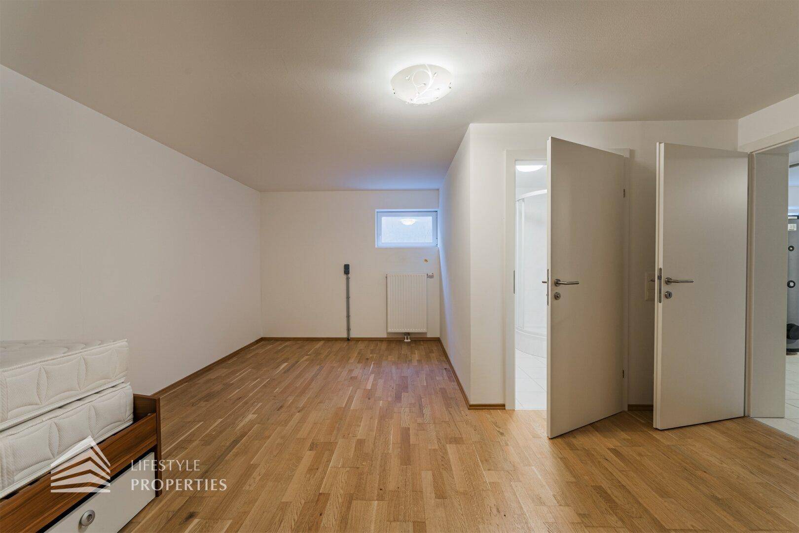 Freundliches Zimmer im Untergeschoss mit Holzfußboden und Zugang zu einem Badezimmer.
