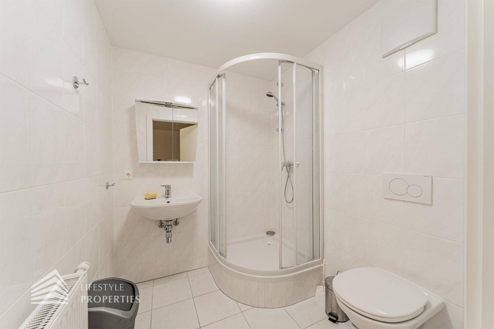 Kleines, hell gefliestes Badezimmer mit Duschkabine, Waschbecken und WC.