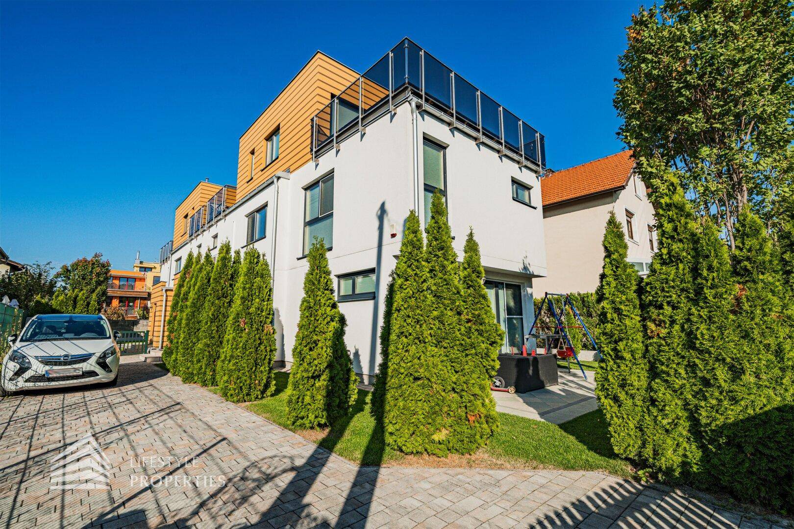 Modernes Einfamilienhaus mit gepflasterter Auffahrt, gepflegter Hecke und viel Grünfläche.