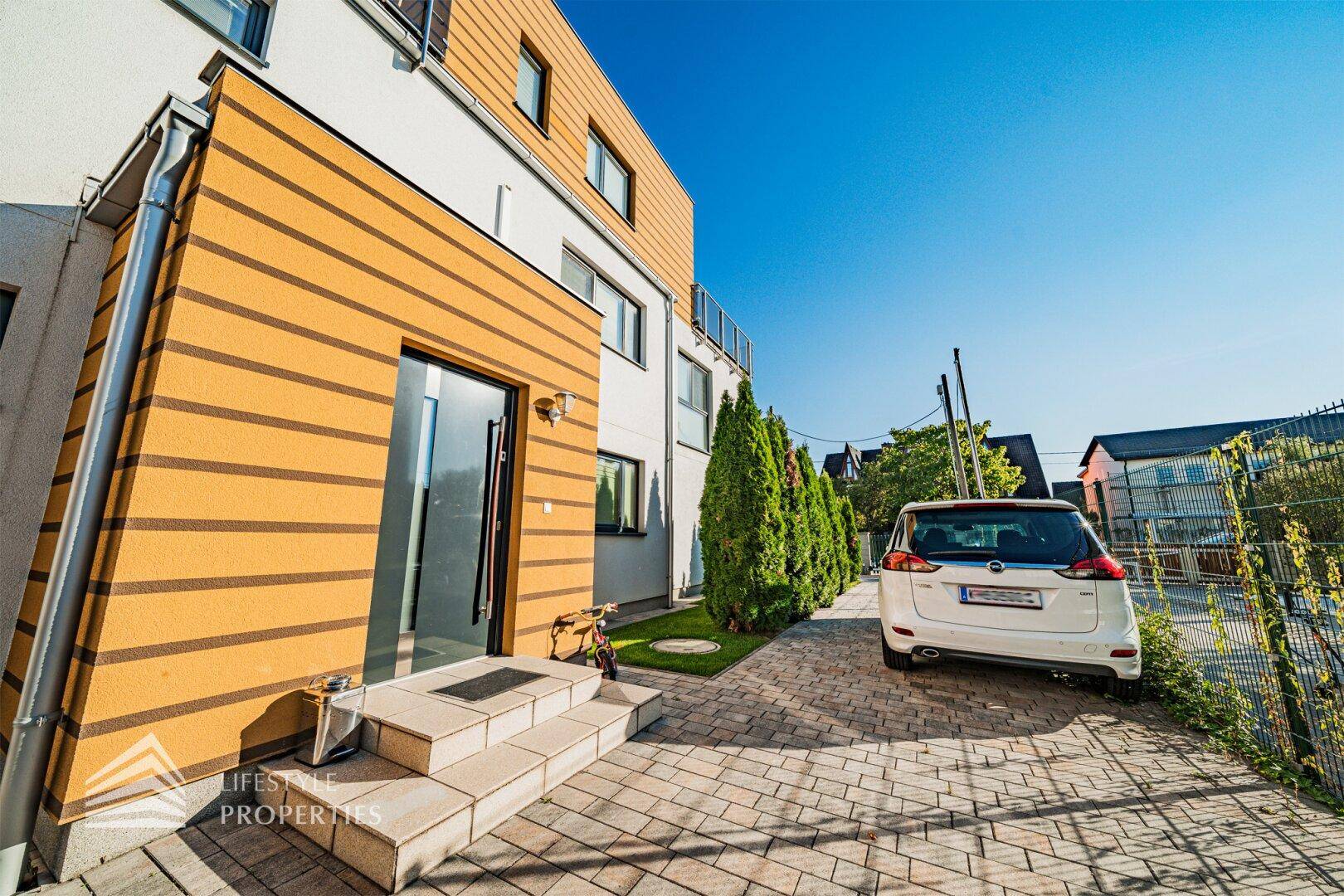 Eingangsbereich des modernen Hauses mit gepflasterter Auffahrt und seitlicher Bepflanzung.