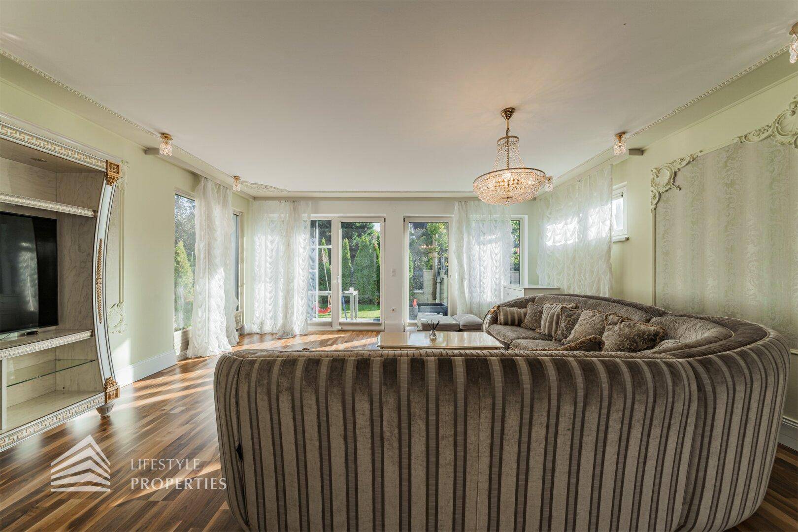 Helles Wohnzimmer mit großem Sofa, Parkettboden, Stuckdecken und Blick in den Garten.