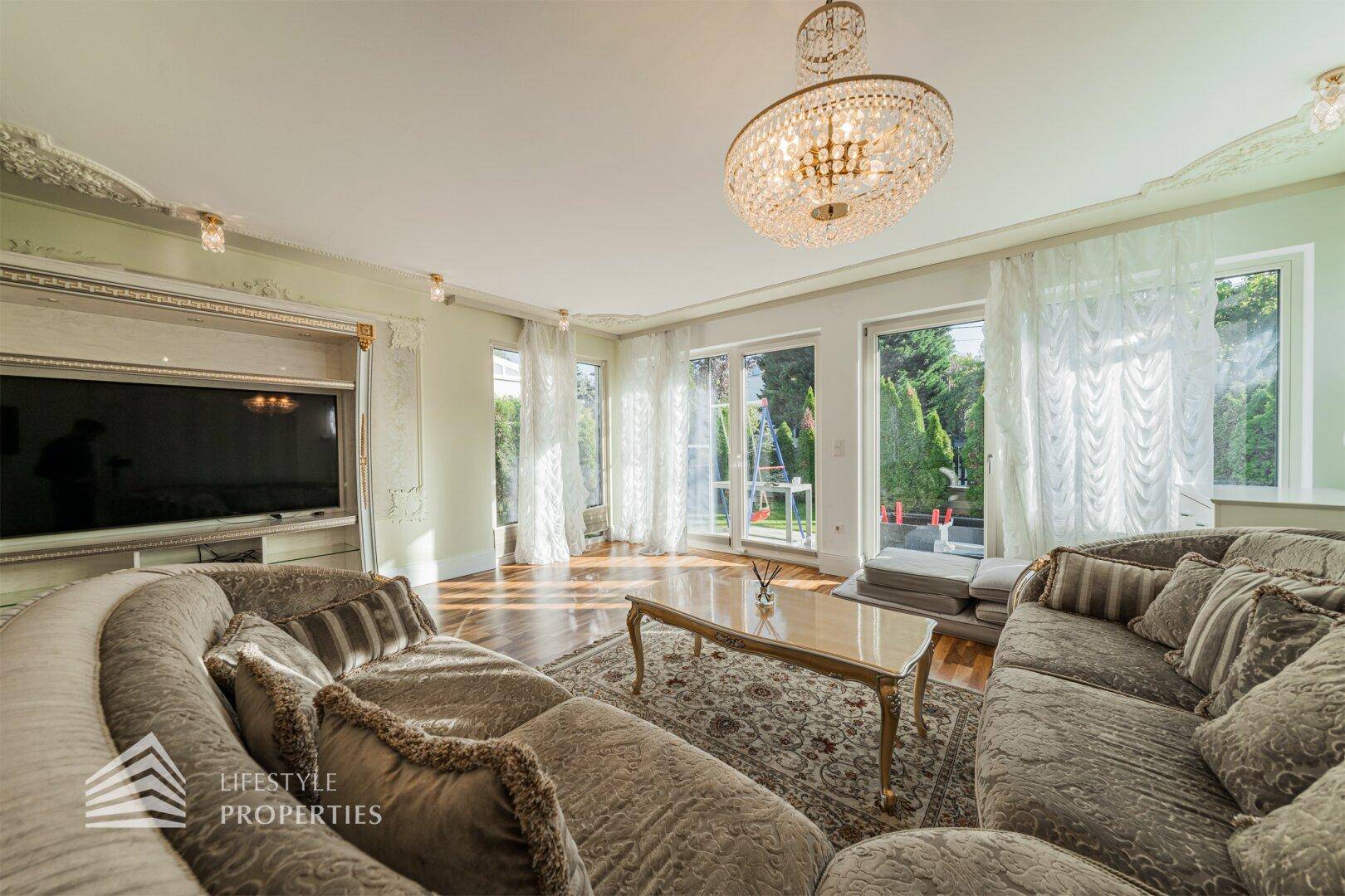 Lichtdurchflutetes Wohnzimmer mit elegantem Sofa, Parkettboden und großen Fenstern zum Garten.