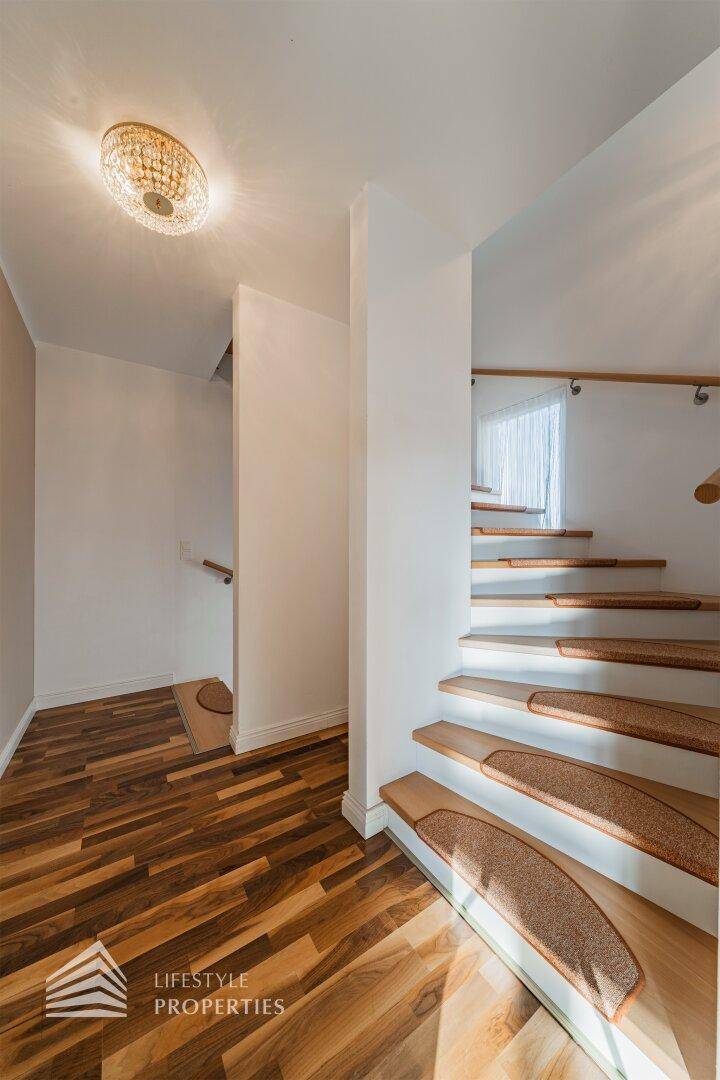 Treppenaufgang mit Parkettboden, heller Wandgestaltung und einem dekorativen Deckenlicht.
