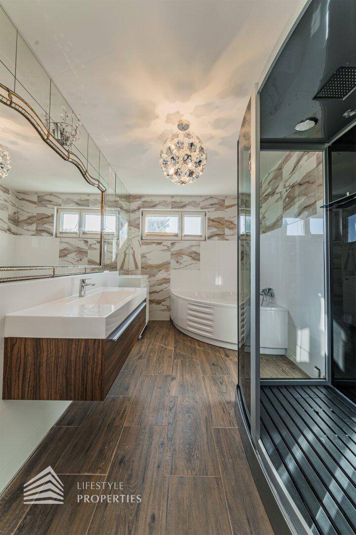 Modernes Badezimmer mit großer Dusche, Eckbadewanne, Doppelwaschbecken und Holzbodenoptik.