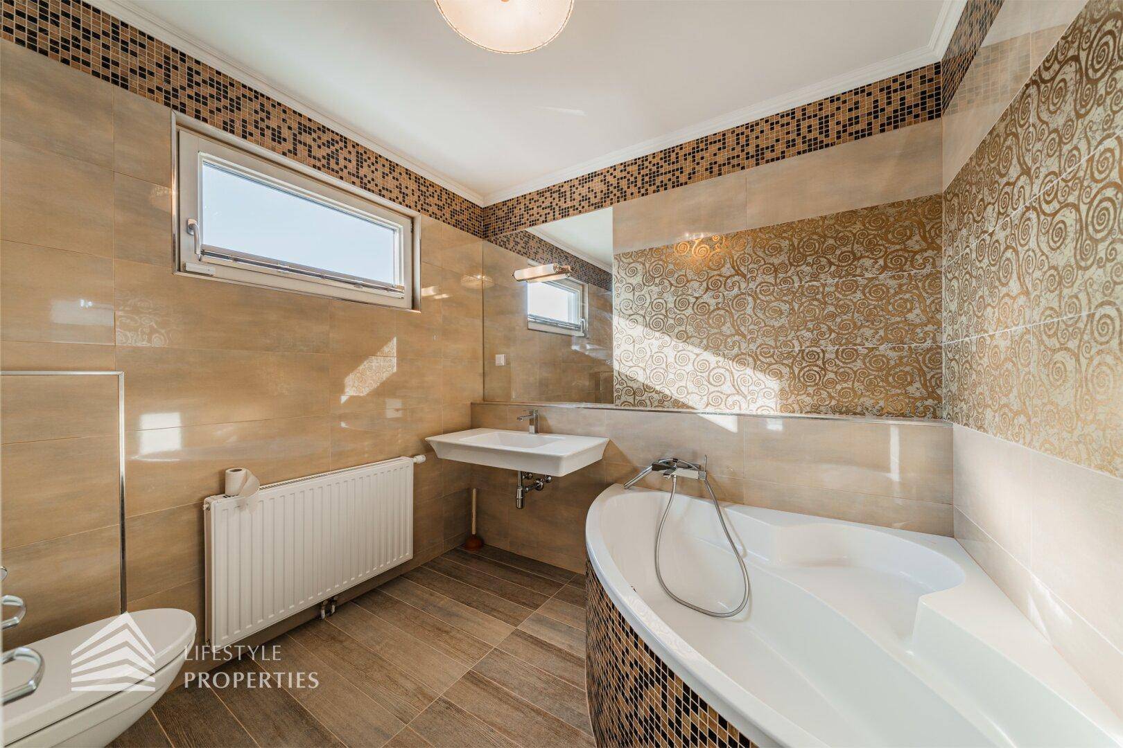 Geräumiges Badezimmer mit Badewanne, WC, Waschbecken und gemusterten Fliesen in Beige.