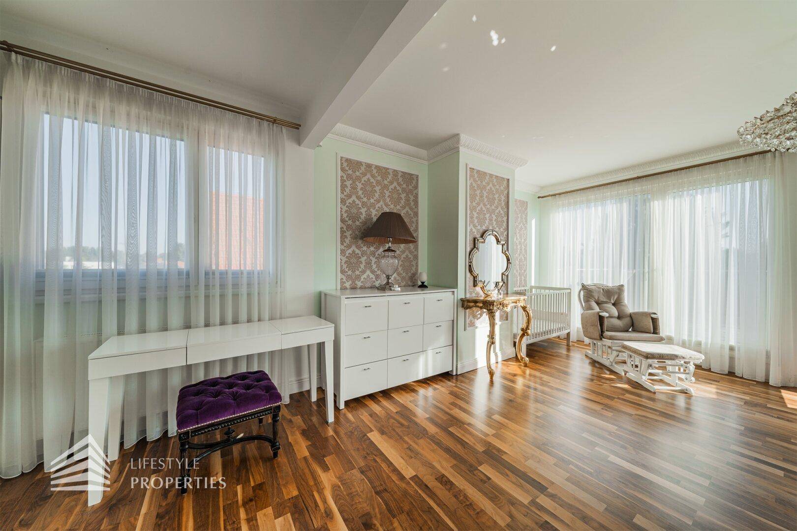 Geräumiges Schlafzimmer mit Parkettboden, hellen Wänden, großen Fenstern und Babybett.