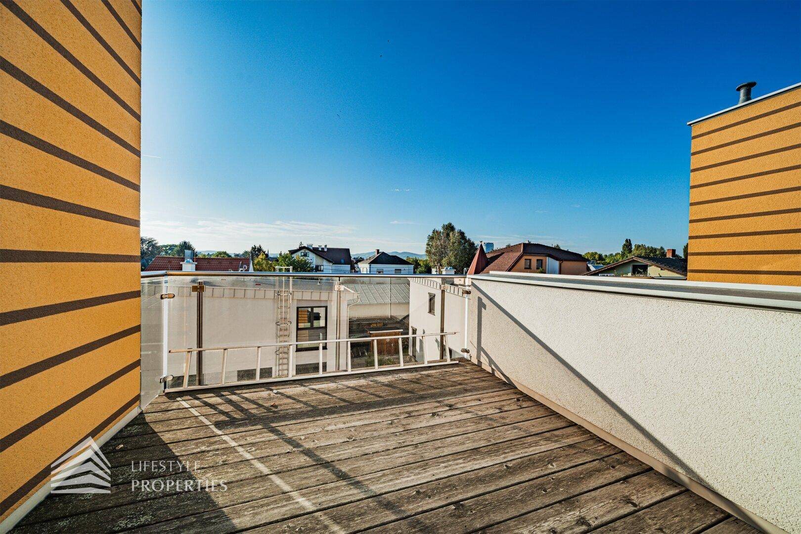 Dachterrasse mit Holzboden und Blick auf die umliegenden Häuser und den klaren blauen Himmel.