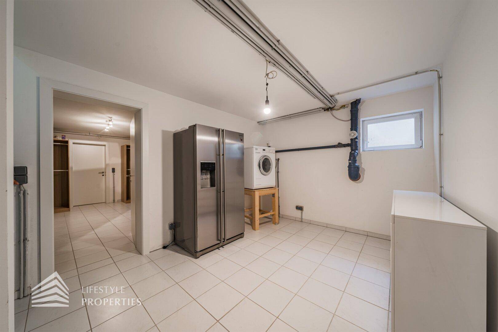 Praktischer Hauswirtschaftsraum im Keller mit Waschmaschine, großem Kühlschrank und Fliesenboden.