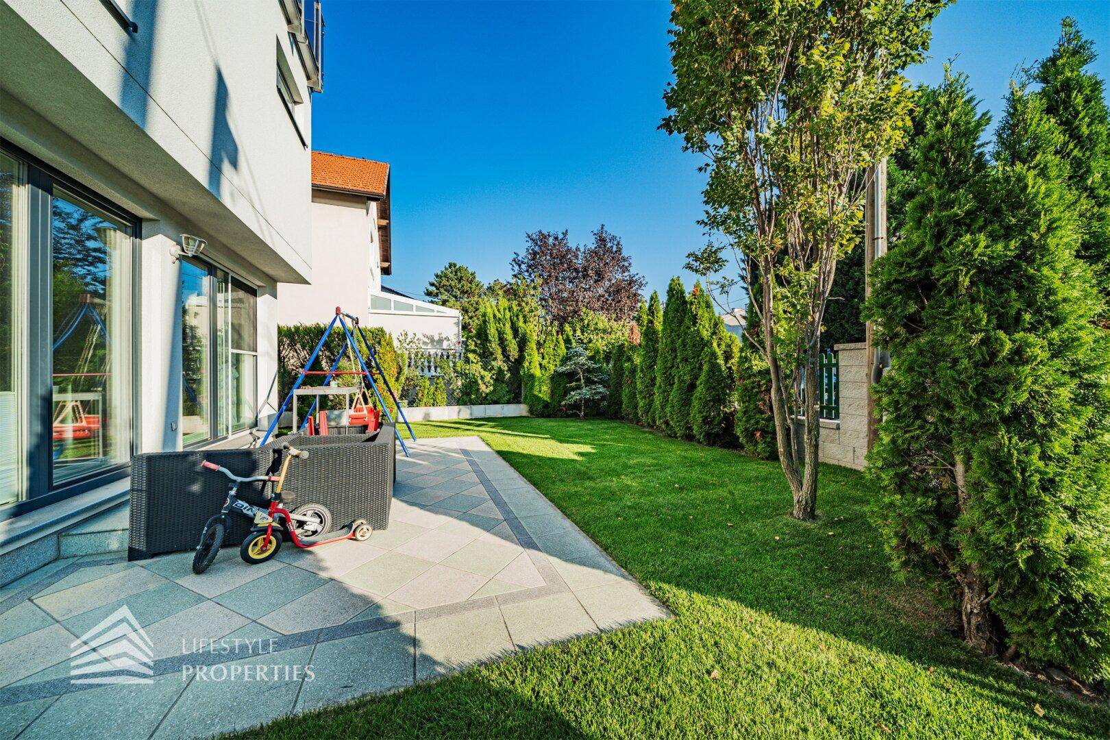 Gepflegter Garten mit Rasenfläche, Terrasse und Kinderschaukel neben dem modernen Haus.