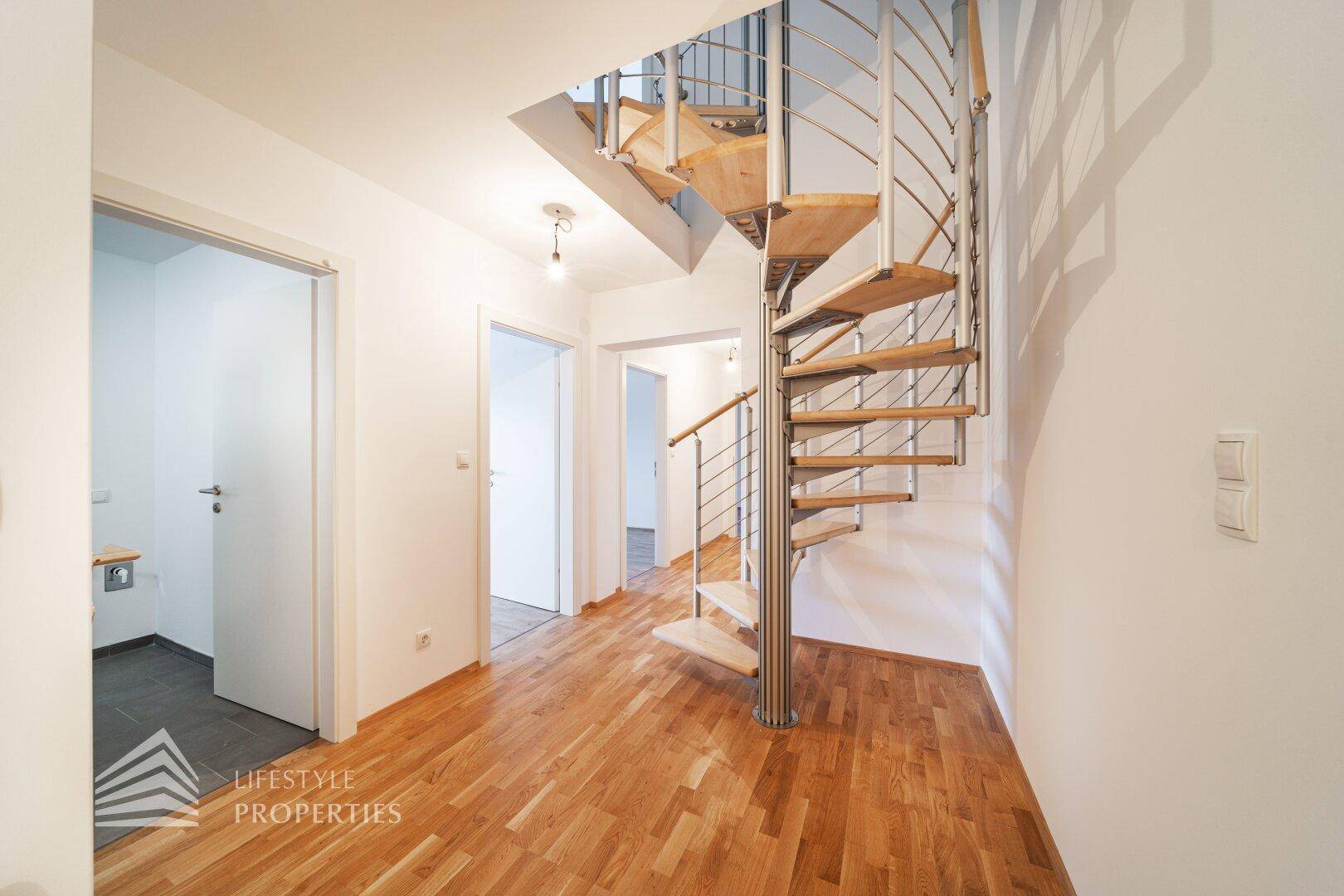 Heller Flur mit eleganter Holz-Metall-Wendeltreppe und Parkettboden.