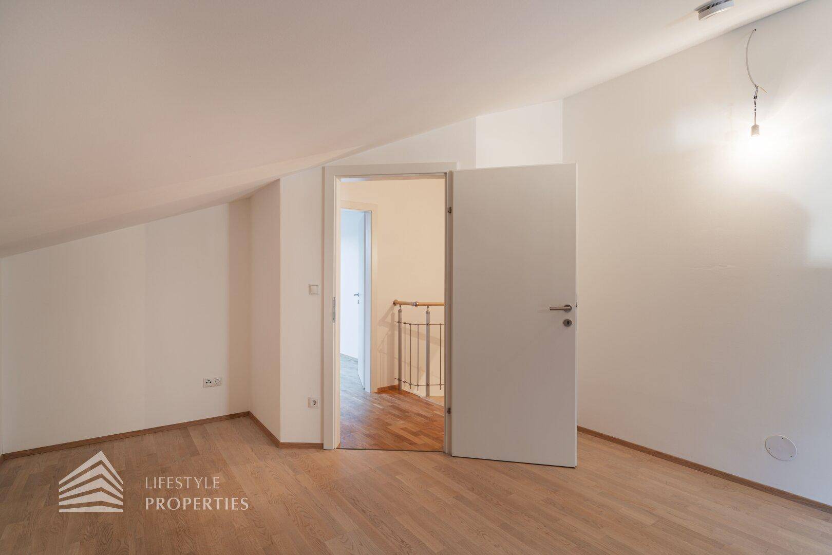 Leeres Zimmer im Dachgeschoss mit Holzboden und Zugang zum Flurbereich.