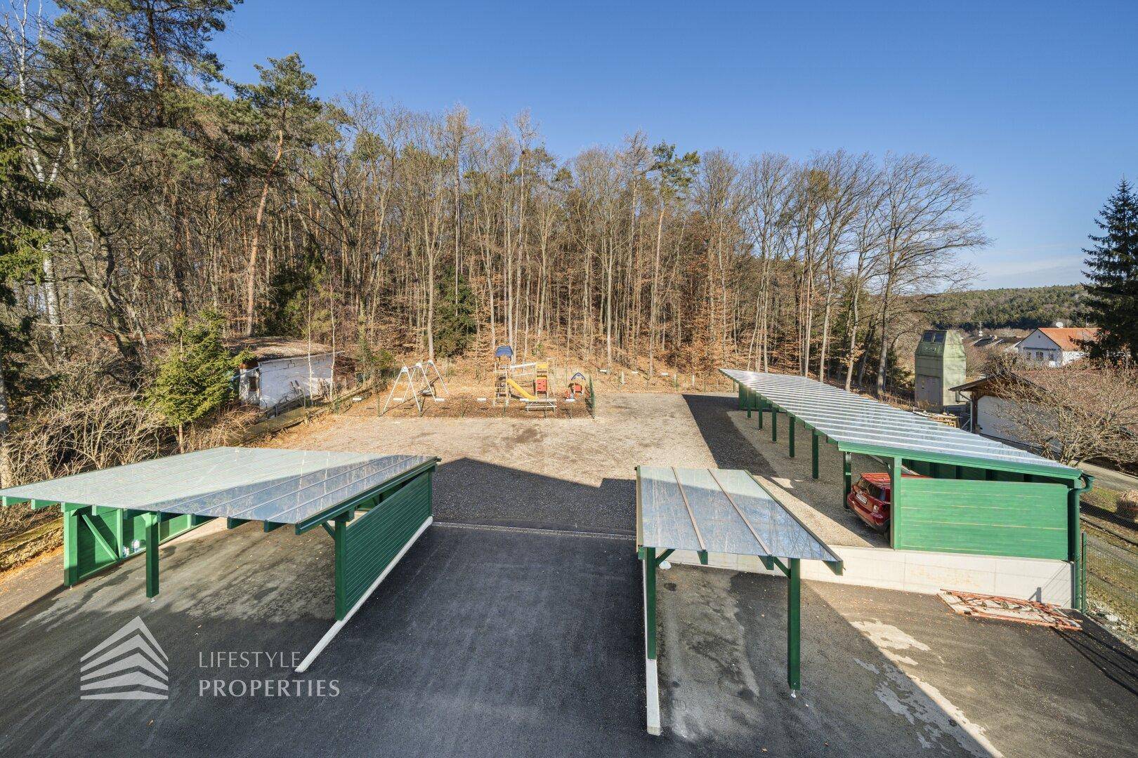 Außenbereich mit mehreren Carports, Parkplätzen und einem Kinderspielplatz.