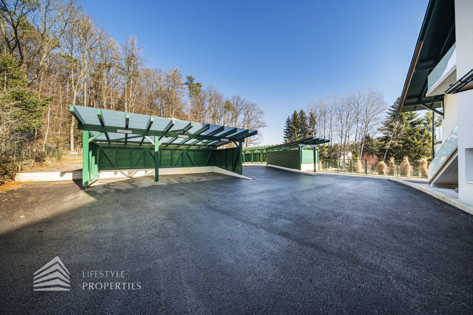 Geräumiger Parkplatz mit überdachten Carports, umgeben von Bäumen.