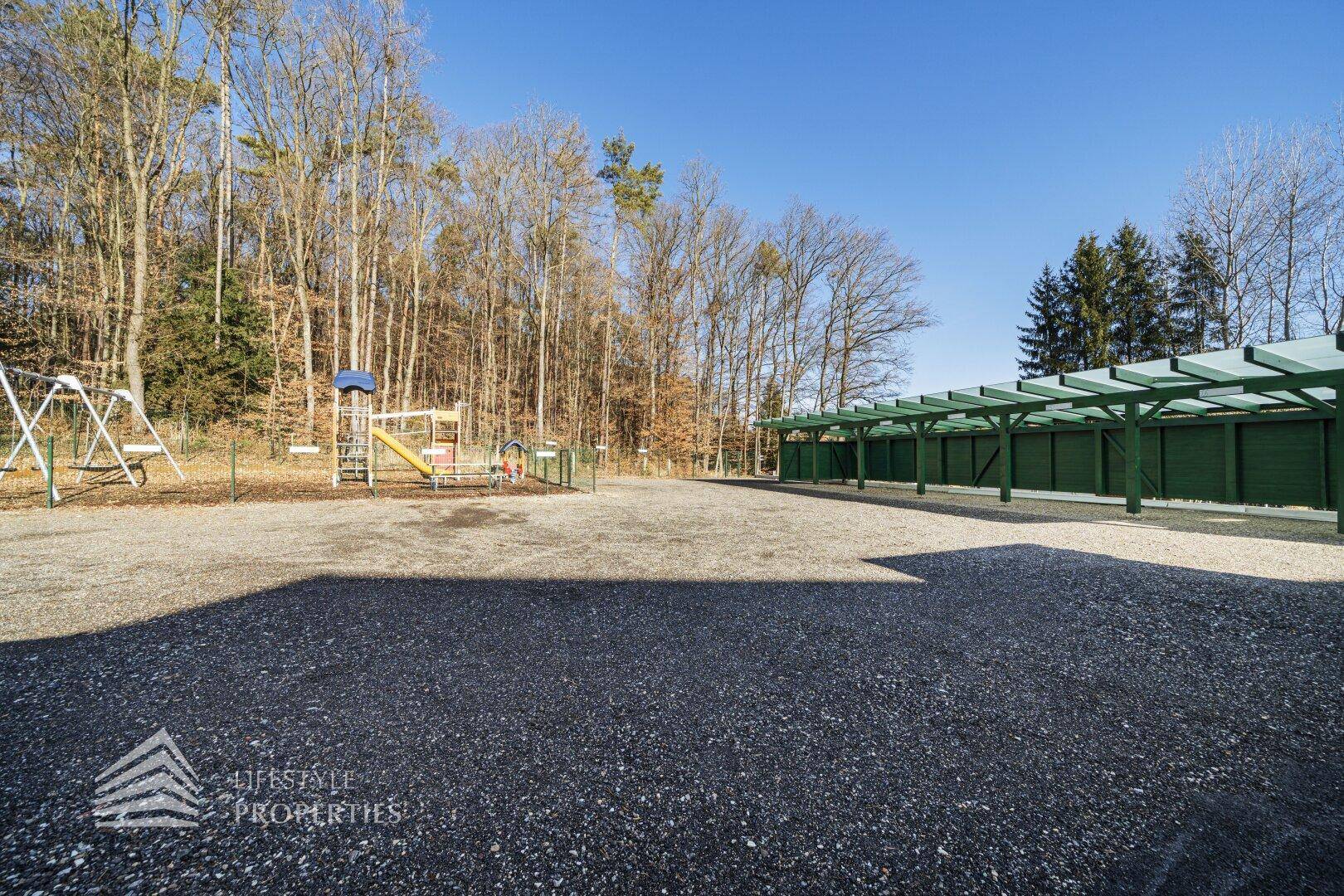 Kinderspielplatz neben dem Parkbereich mit Carports und Waldrand.