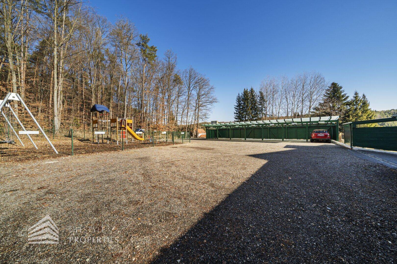 Weitläufiger Außenbereich mit Spielplatz und überdachten Parkplätzen.