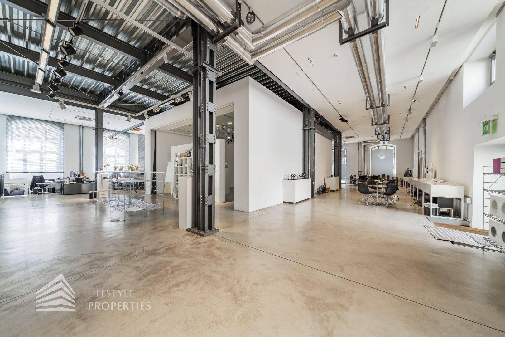 Weitläufiger Büroraum mit industriellem Design, Betonboden und freiliegenden Rohren an der Decke.