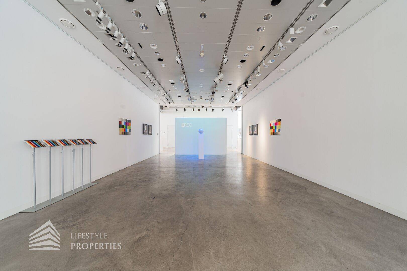 Moderner Ausstellungsraum mit Betonboden, minimalistischer Einrichtung und Kunstwerken an den Wänden.