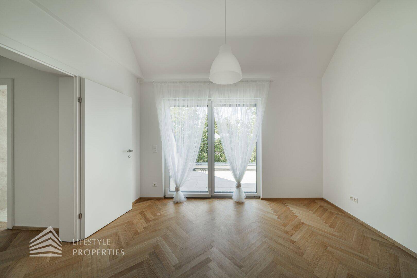 Geräumiges Schlafzimmer mit Fischgrätparkett und großen Fenstern, die viel Licht hereinlassen.