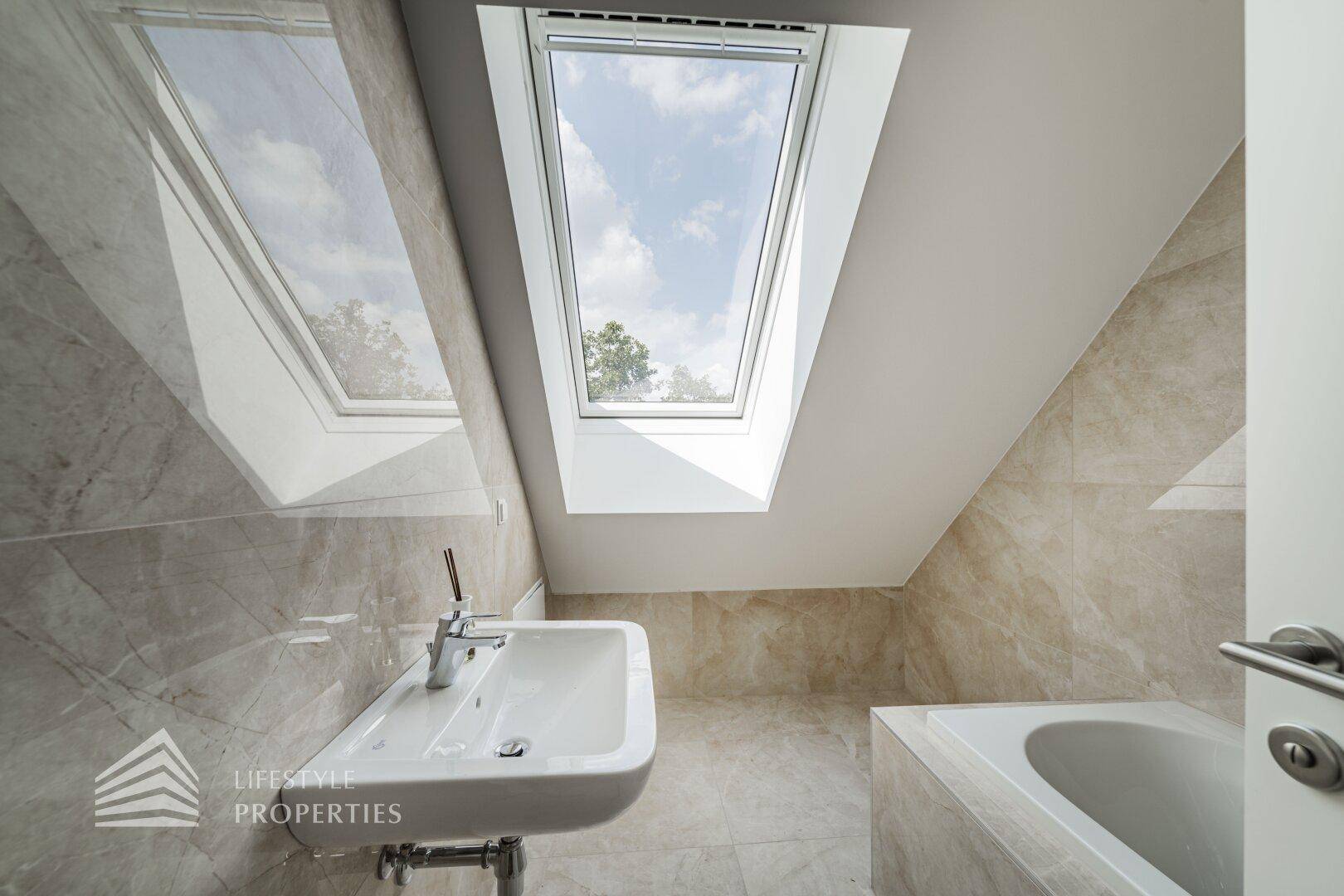 Modernes Badezimmer mit beigefarbenen Fliesen, Badewanne und einem Dachfenster für Tageslicht.
