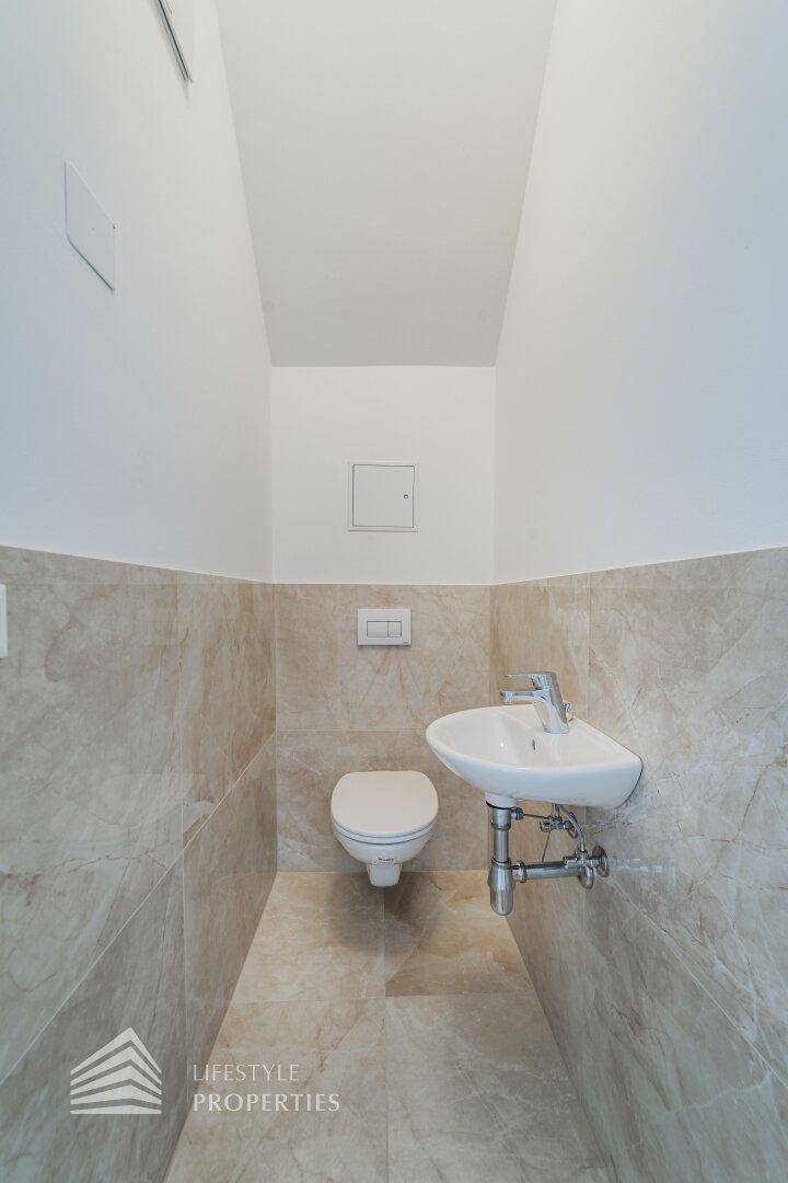 Gäste-WC mit modernen beigefarbenen Fliesen, wandhängendem WC und kleinem Waschbecken.