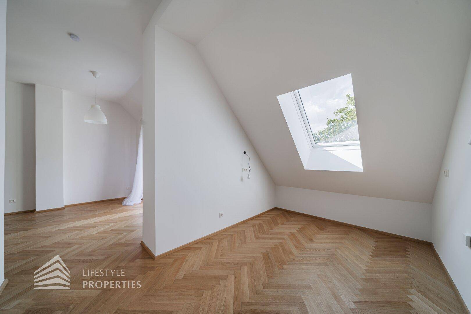 Dachgeschosszimmer mit schrägen Wänden, Fischgrätparkett und einem Dachfenster für natürliches Licht.