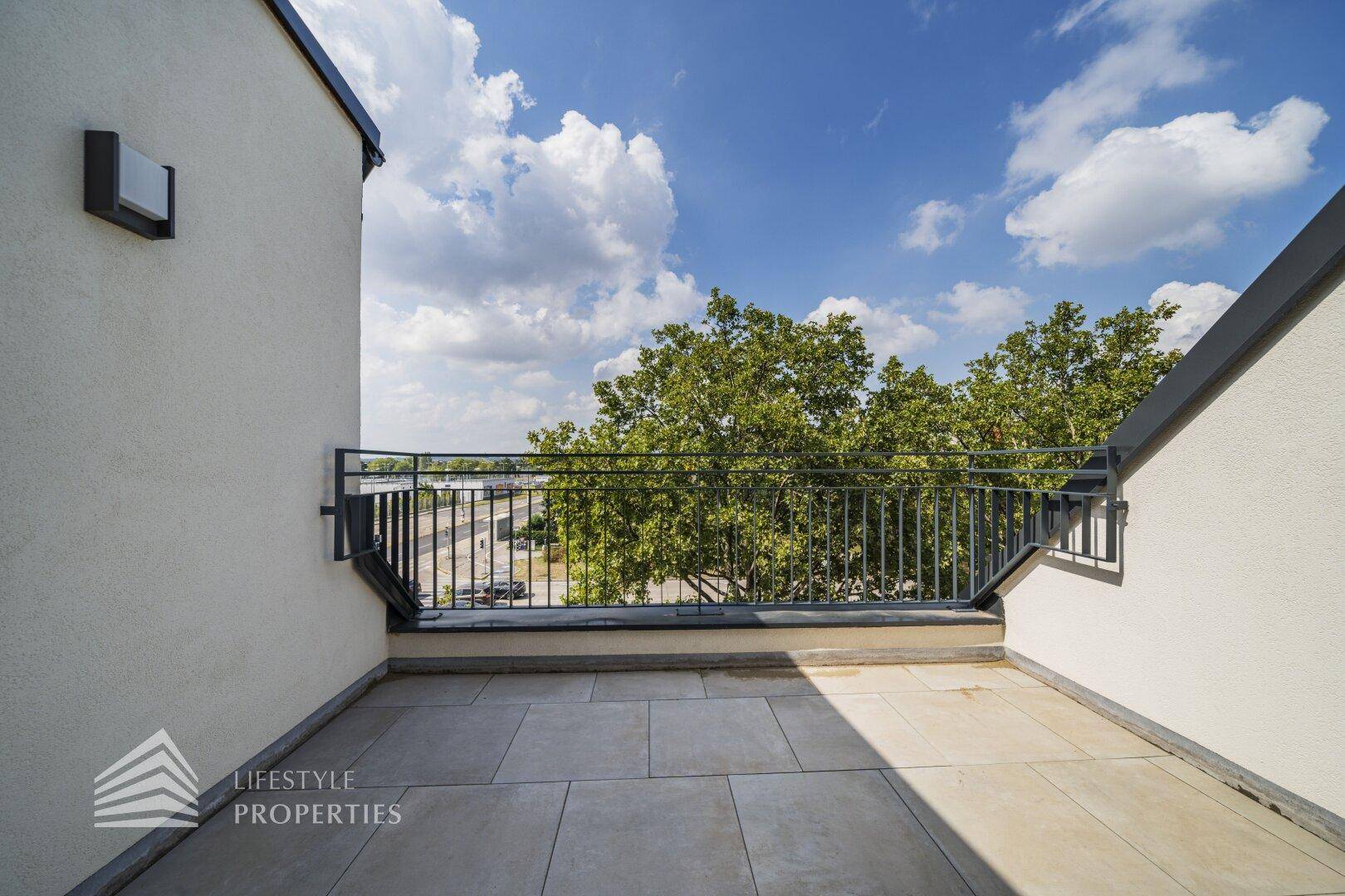 Geräumige Dachterrasse mit Fliesenboden und Blick auf die Umgebung und Bäume.