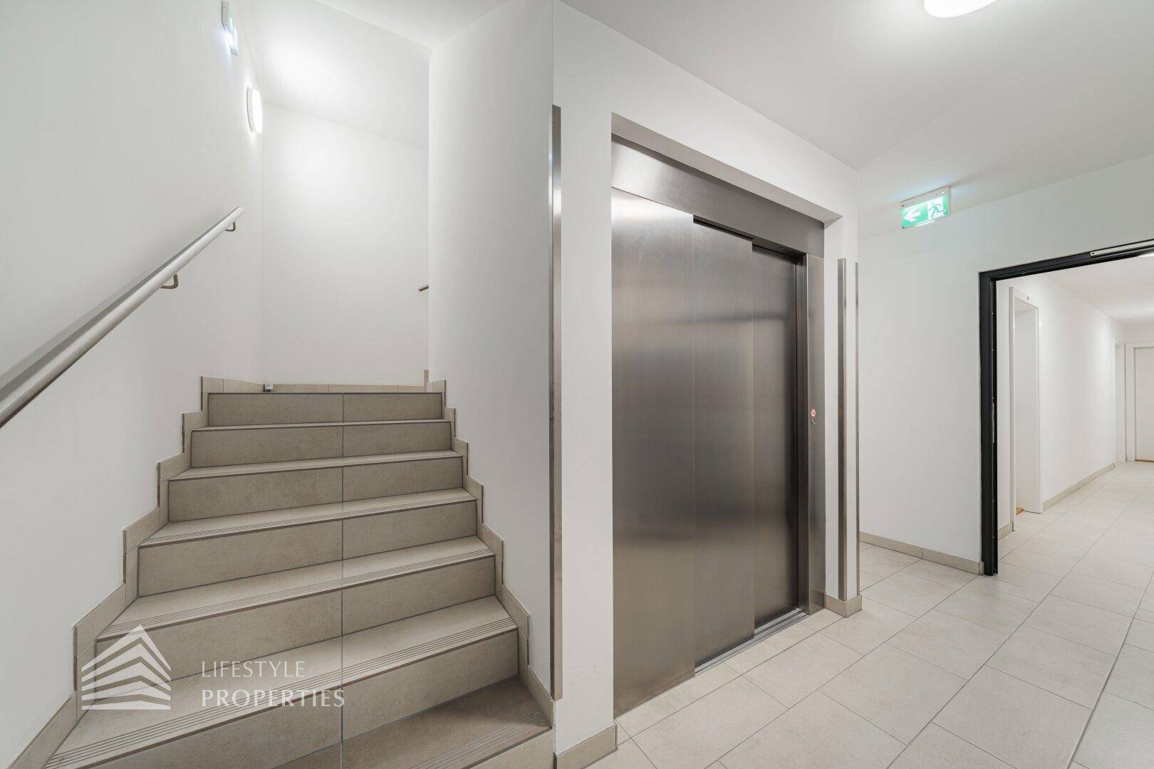 Heller Treppenaufgang und Flur mit Aufzug in einem modernen Mehrfamilienhaus.