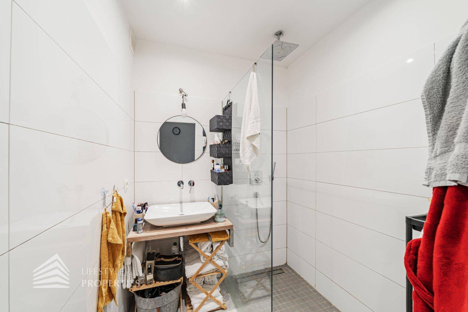 Modernes Badezimmer mit ebenerdiger Dusche, stilvollem Waschbecken und weißen Fliesen.