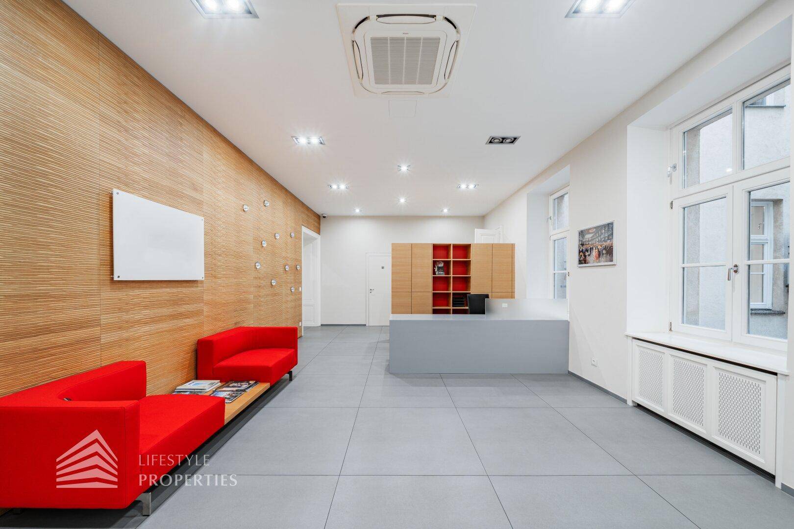 Moderner Empfangsbereich mit roten Sofas, einer Holzwand und grauen Bodenfliesen.