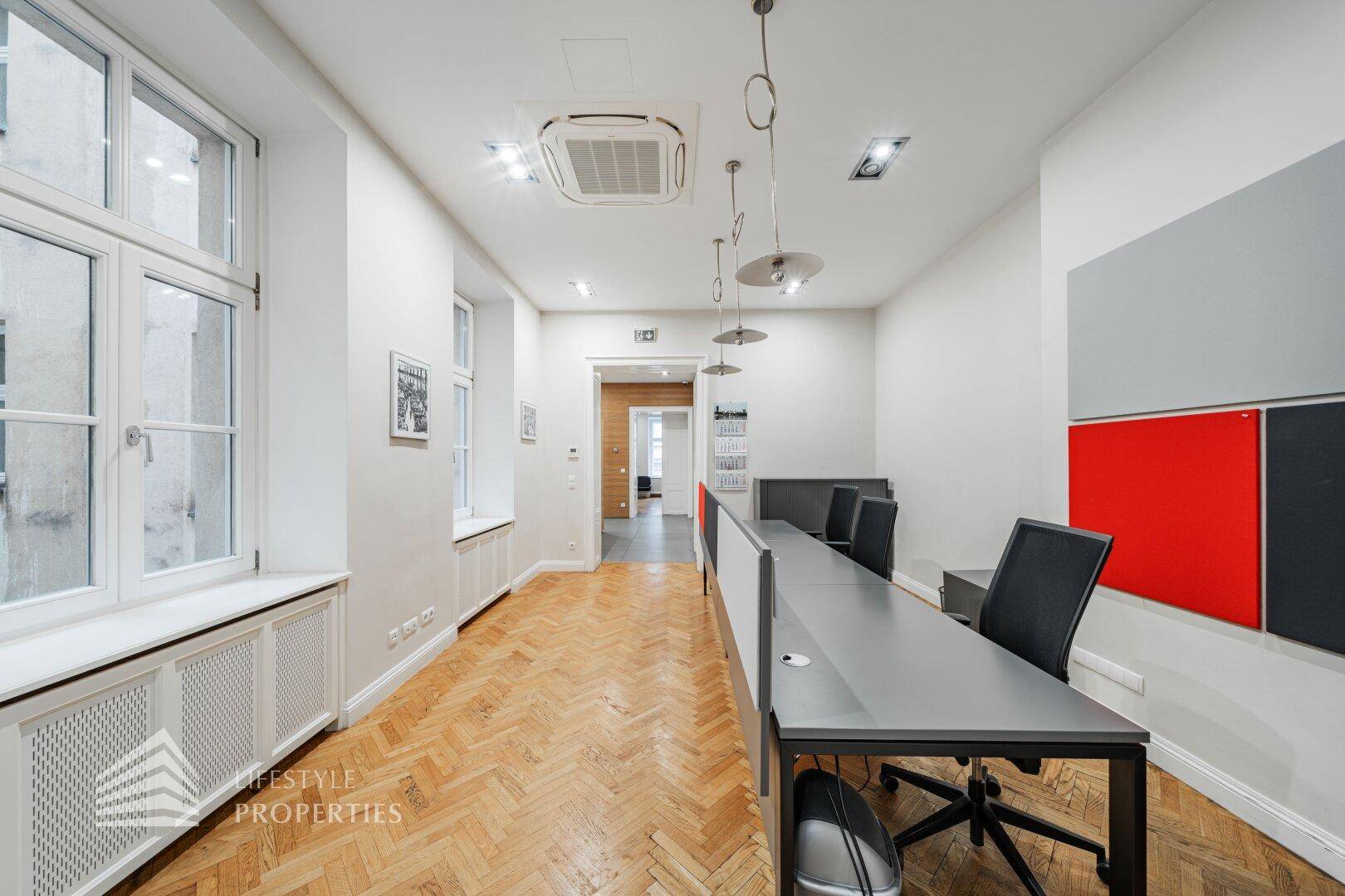 Modernes Büro mit Reihen von Schreibtischen, roten Akzenten und hellem Fischgrätparkett.
