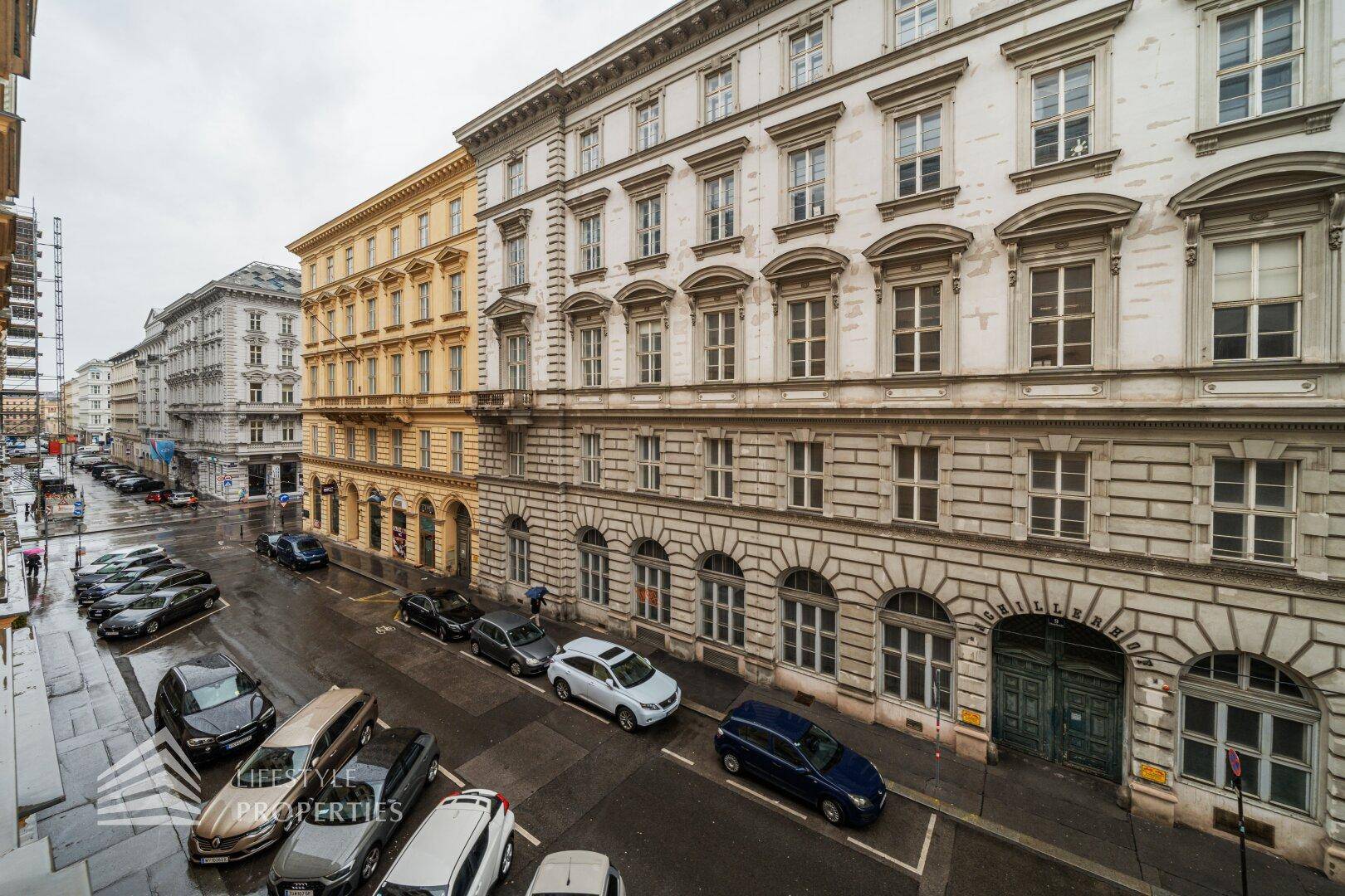 Historisches Gebäude an einer belebten Straße mit parkenden Autos und klassischer Architektur.