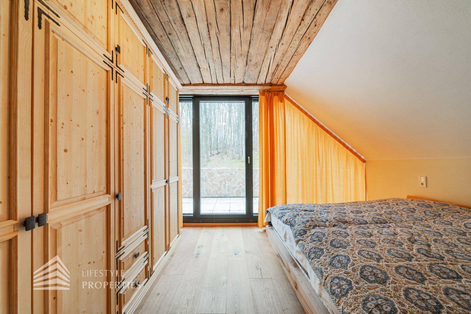 Gemütliches Schlafzimmer mit Holzdecke, Einbauschränken und Zugang zum Außenbereich.