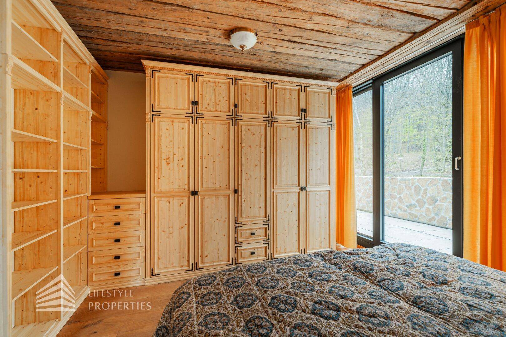 Schlafzimmer mit Holzdecke, Einbauschränken und Fenster mit Blick ins Grüne.