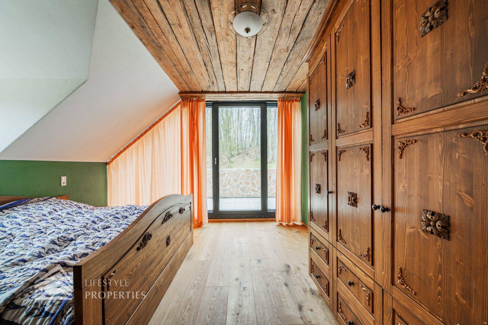 Schlafzimmer mit dunklen Holzmöbeln, Holzboden und Zugang zu einem Balkon oder Terrasse.