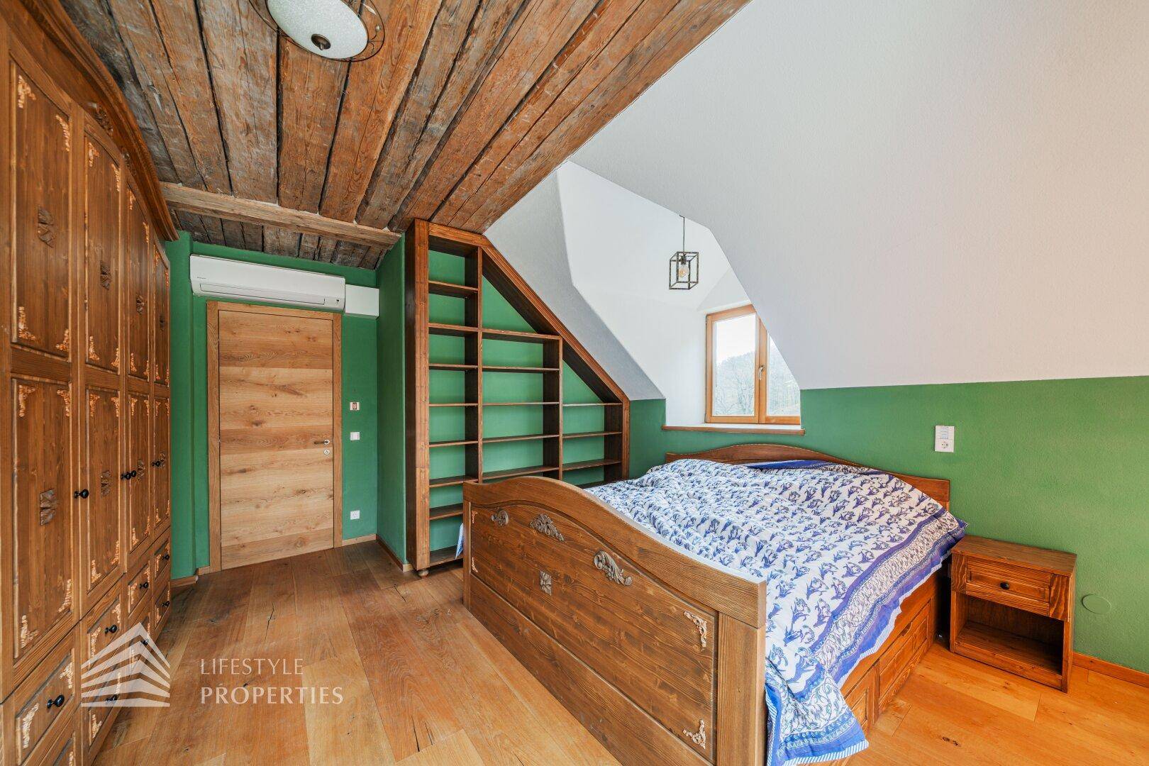 Schlafzimmer mit grünen Wänden, Holzboden und rustikalen Holzmöbeln unter Dachschräge.