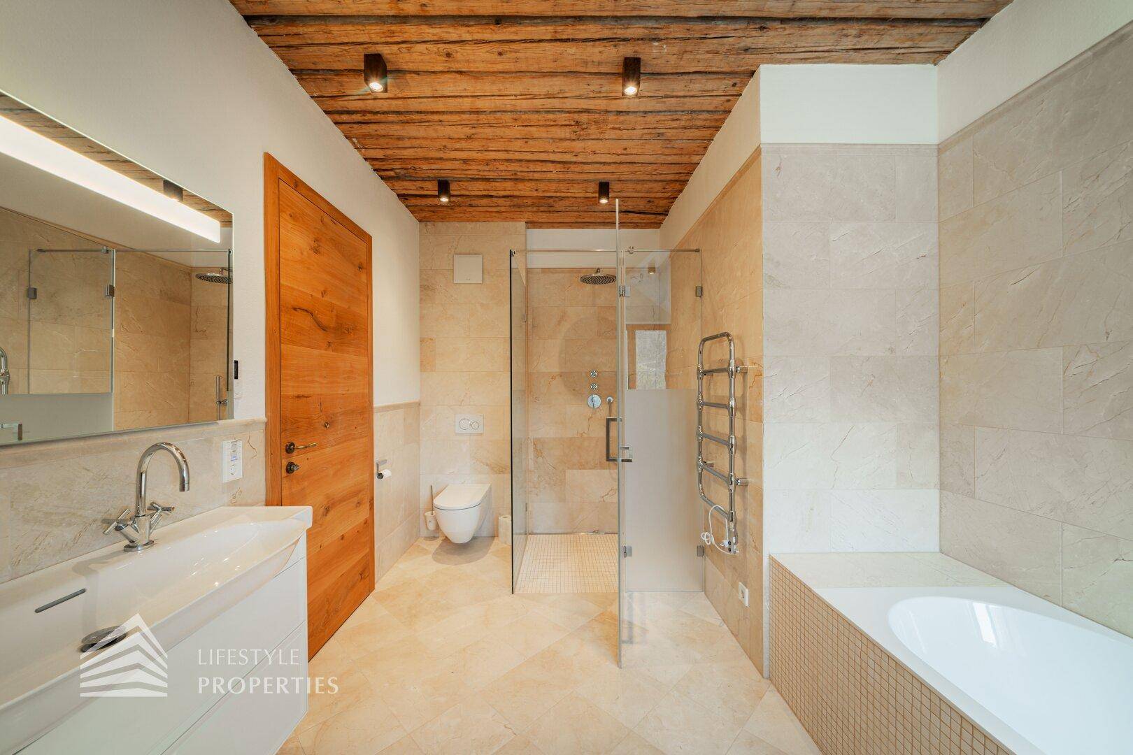 Helles Badezimmer mit beigen Fliesen, Dusche, Waschtisch und Holzdecke.