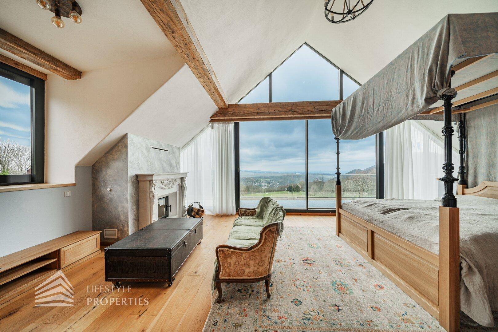 Helles Schlafzimmer mit Himmelbett, Kamin und großen Fenstern mit Panoramablick.