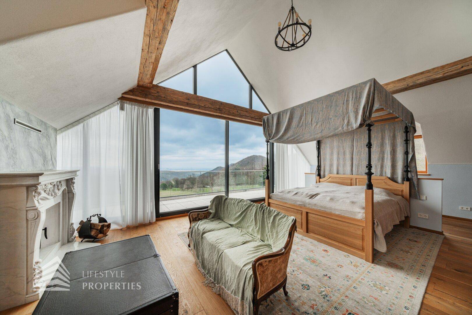 Geräumiges Schlafzimmer mit Himmelbett, Kamin und raumhohen Fenstern mit weitem Ausblick.