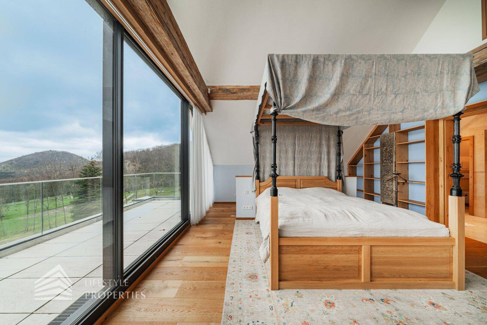 Helles Schlafzimmer mit Holzboden, Himmelbett und raumhohen Fenstern mit weitem Ausblick.