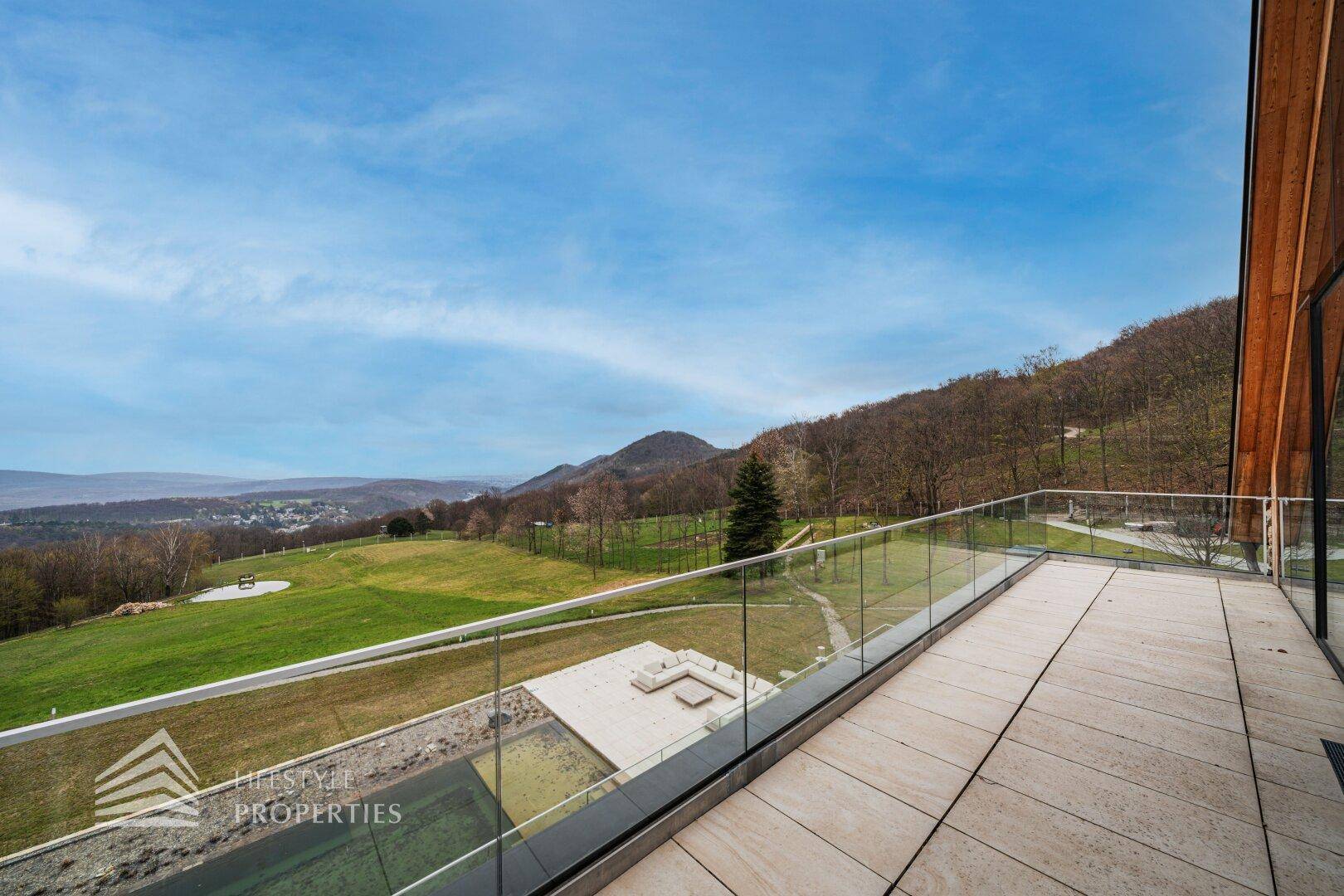 Obere Terrasse mit Glasgeländer und atemberaubendem Weitblick über die grüne Hügellandschaft.