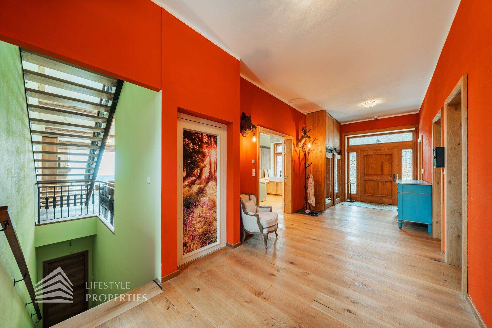 Geräumiger Eingangsbereich mit orangefarbenen Wänden, Holzboden und Treppenaufgang.