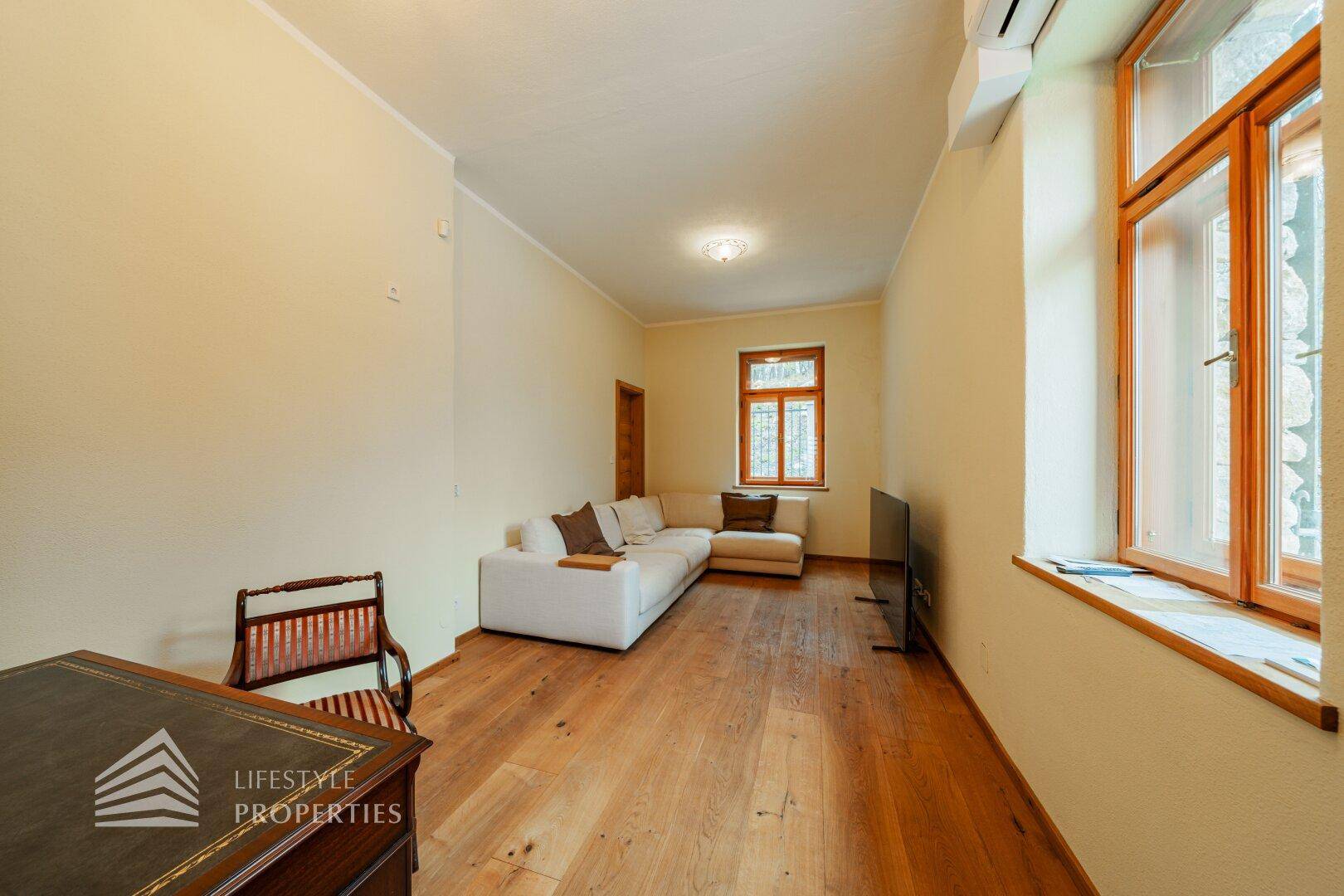 Helles Wohnzimmer mit Holzboden, weißem Sofa und Fenstern mit Blick nach draußen.