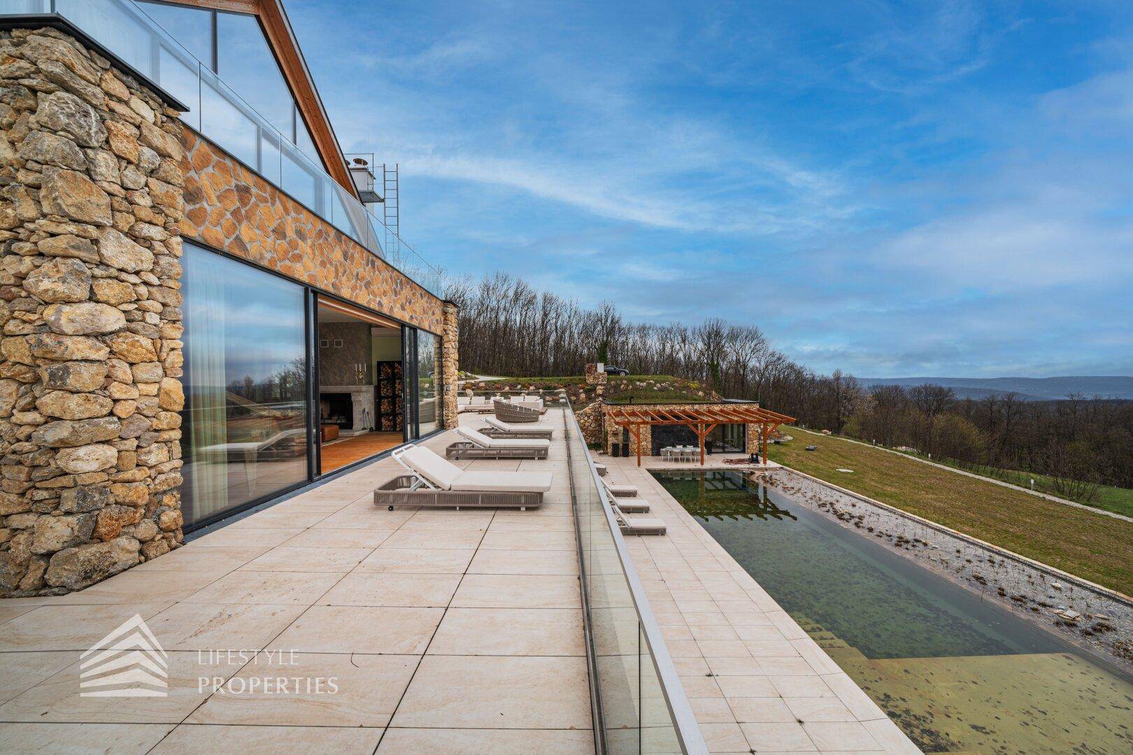 Große Terrasse mit Liegestühlen, Pool und weitem Blick über die hügelige Landschaft und Natur.