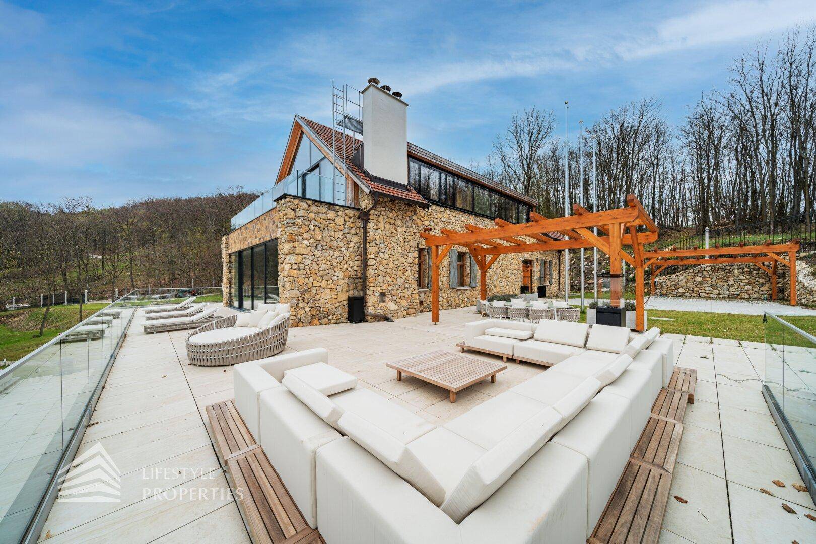 Weitläufige Terrasse mit bequemen Outdoor-Sitzmöbeln, Pergola und Blick auf die umliegende Natur.