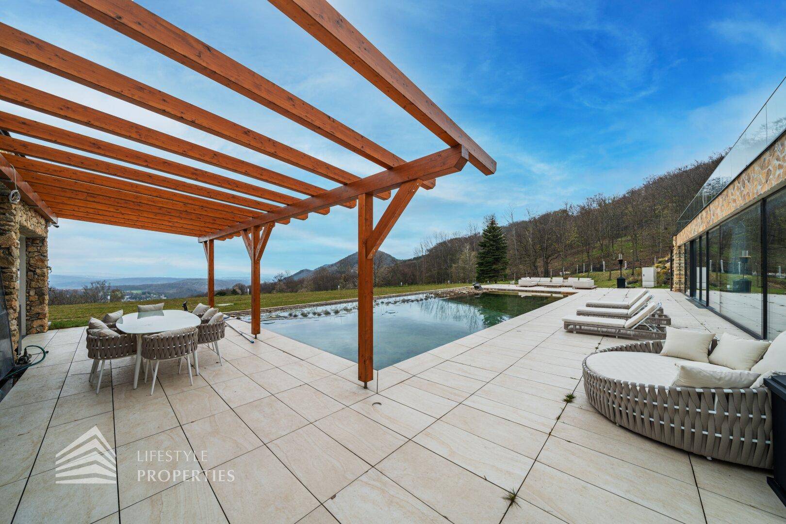 Elegante Terrasse mit Essbereich unter einer Pergola, Pool und Liegeflächen mit Panoramablick.
