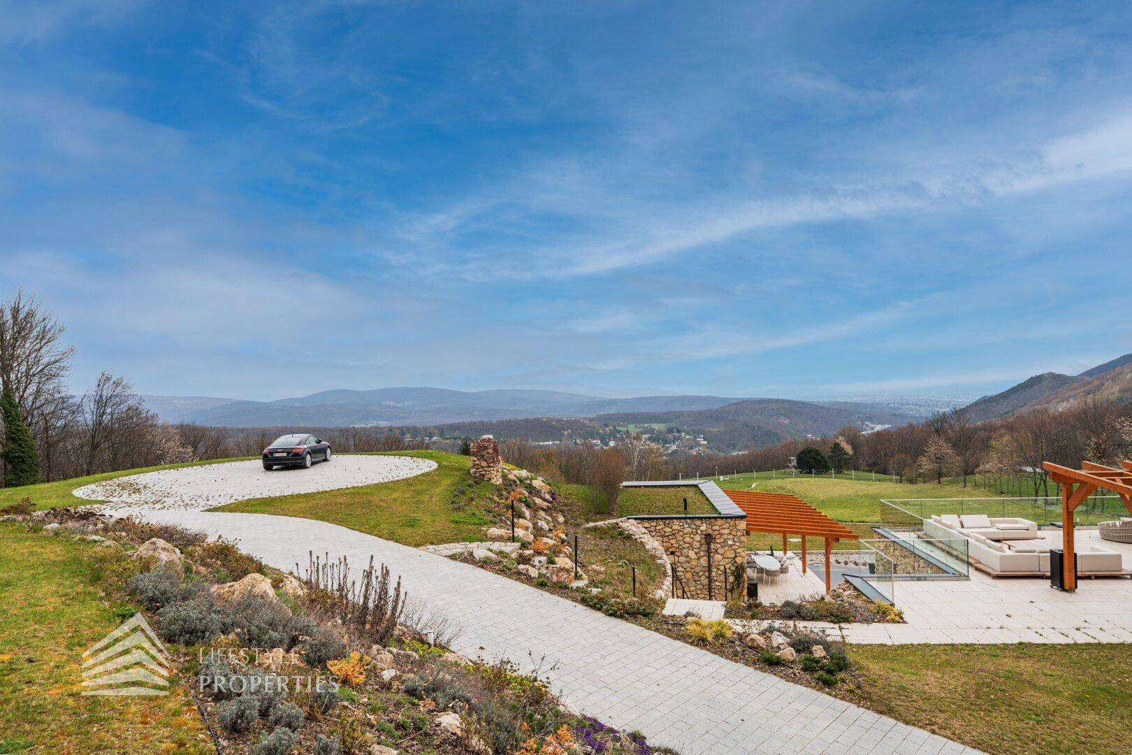 Geschwungene Auffahrt zum Anwesen mit Panoramablick auf die umliegende hügelige Landschaft.