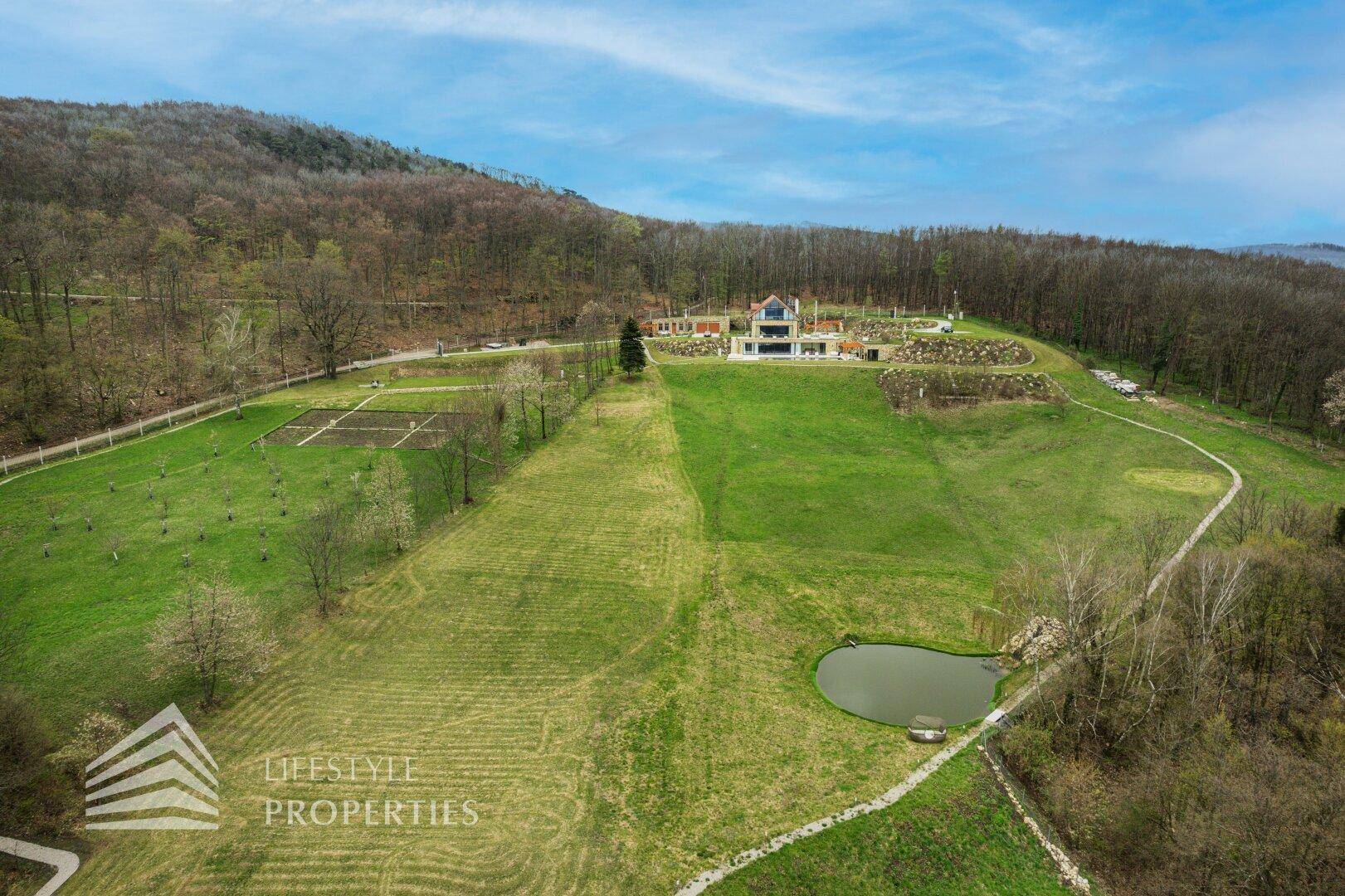 Weitläufige Luftaufnahme des Anwesens mit Villa, Pool, Teich und weitläufigen Grünflächen.