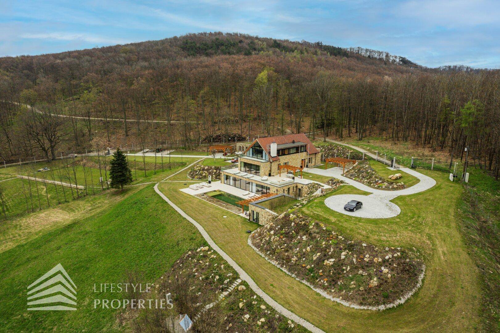 Luftaufnahme der Villa mit Poolbereich, geschwungener Auffahrt und umgebender Hügellandschaft.